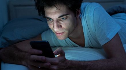 Ragazzo con smartphone a letto e luce blu