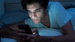 Ragazzo con smartphone a letto e luce blu