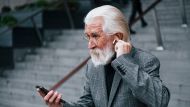 Anziano elegante signore preme auricolare nell’orecchio