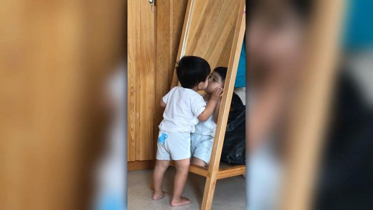 Il bambino sbaciucchia la sua immagine riflessa