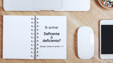 A dx, scritta “Si scrive deficente o deficiente? Scopri come si scrive...” su quaderno bianco a spirale posato su tavolo in legno; a dx, mouse; sopra, parte di tastiera di pc