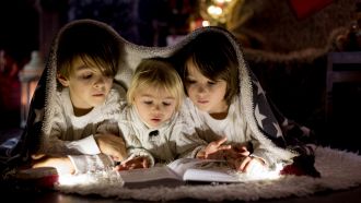 Tre bambini di 3, 4 e 5 anni leggono sotto una coperta