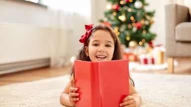 Distesa su un tappeto bianco, una solare bambina di 4 anni tiene tra le mani un grande libro dalla copertina rossa mentre guarda l'obiettivo