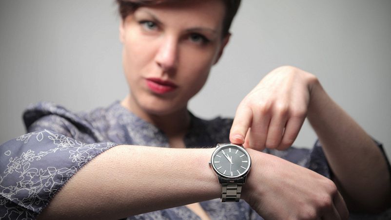 Donna che indica il proprio orologio per sottolineare un ritardo