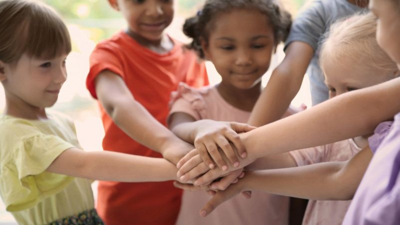Bambine bionde, castane e dai capelli scuri, caucasiche e africane uniscono le loro mani poggiandole le une sulle altre. Inclusione, rispetto, tolleranza