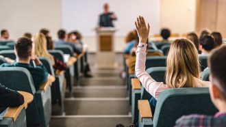 Rear view of college student raising her hand in amphitheater.