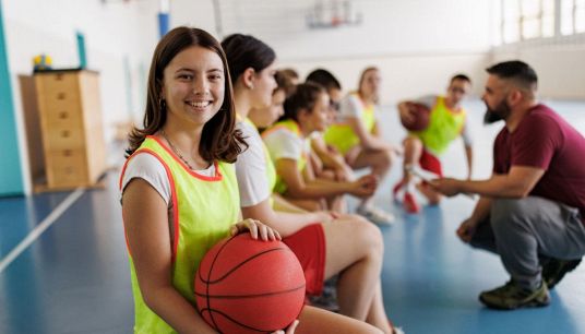 ragazza con pallone da pallacanestro in un gruppo con un insegnante